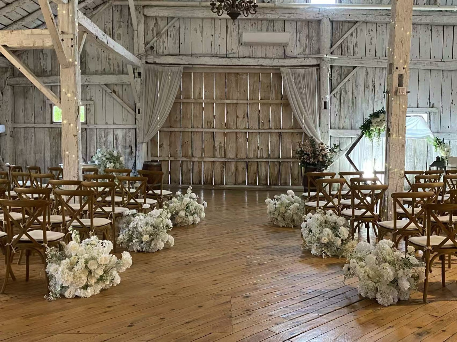 A barn with wooden chairs and flowers along the aisle.