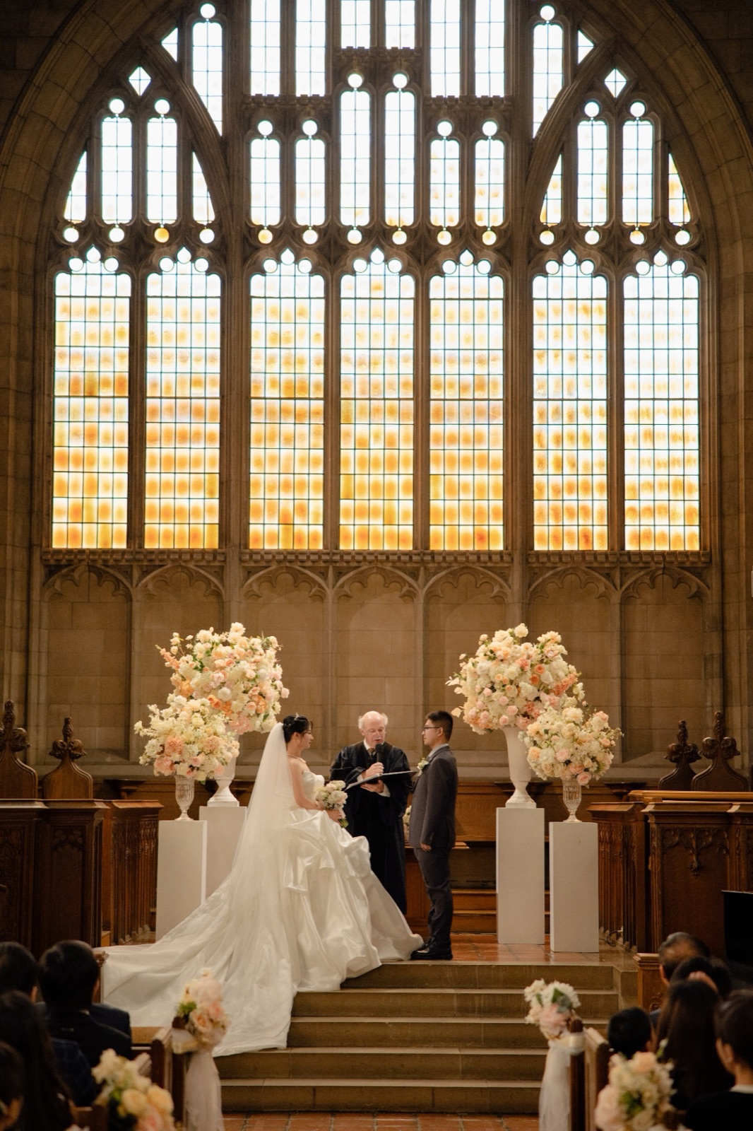 A ceremony at the altar beneath a tall stained-glass window.