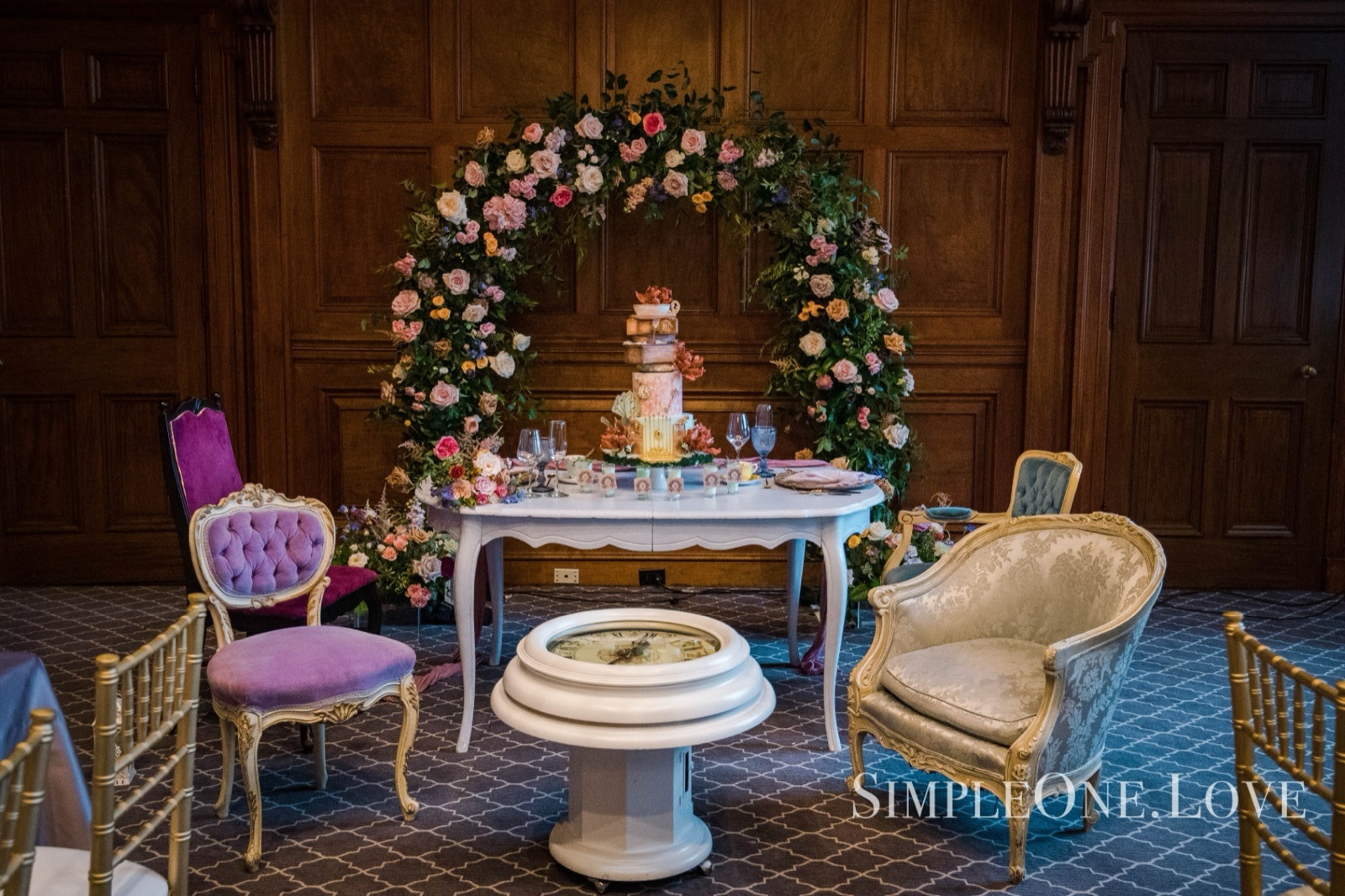 A sweetheart table and floral arch in a panelled room.