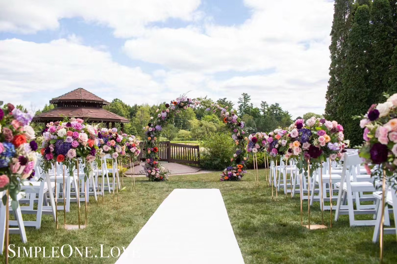 A garden ceremony with a white aisle and flower-lined chairs.